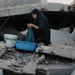 Mulher lava roupas entre escombros em Gaza.